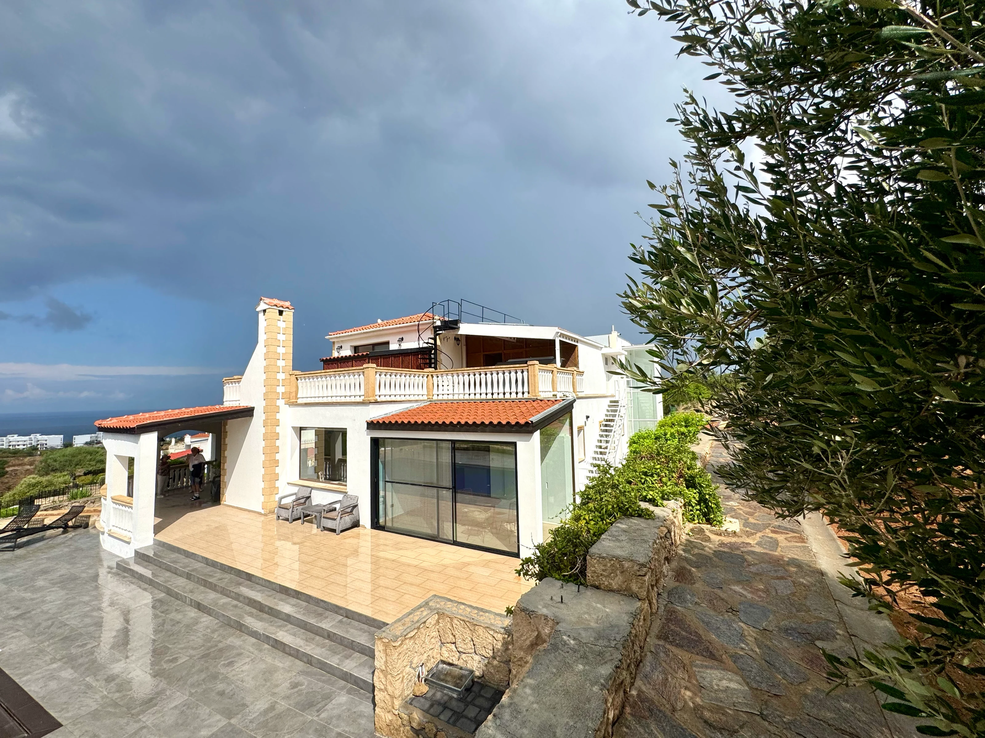 Main villa with stone tower, covered balcony and glass terrace, beside an olive tree